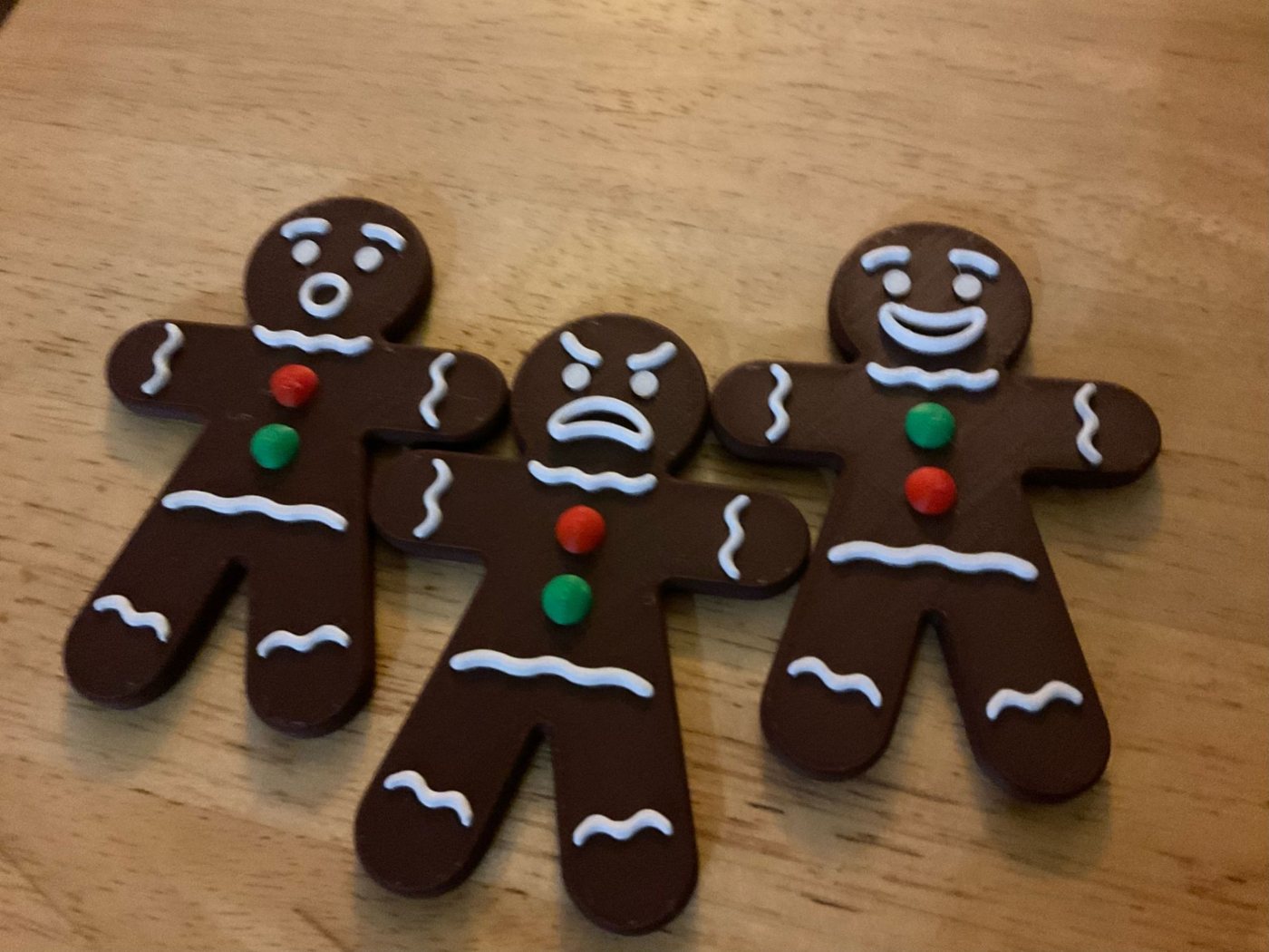 Three flat gingerbread figures with white icing lines and red and green buttons, one surprised, one cross and one smiling