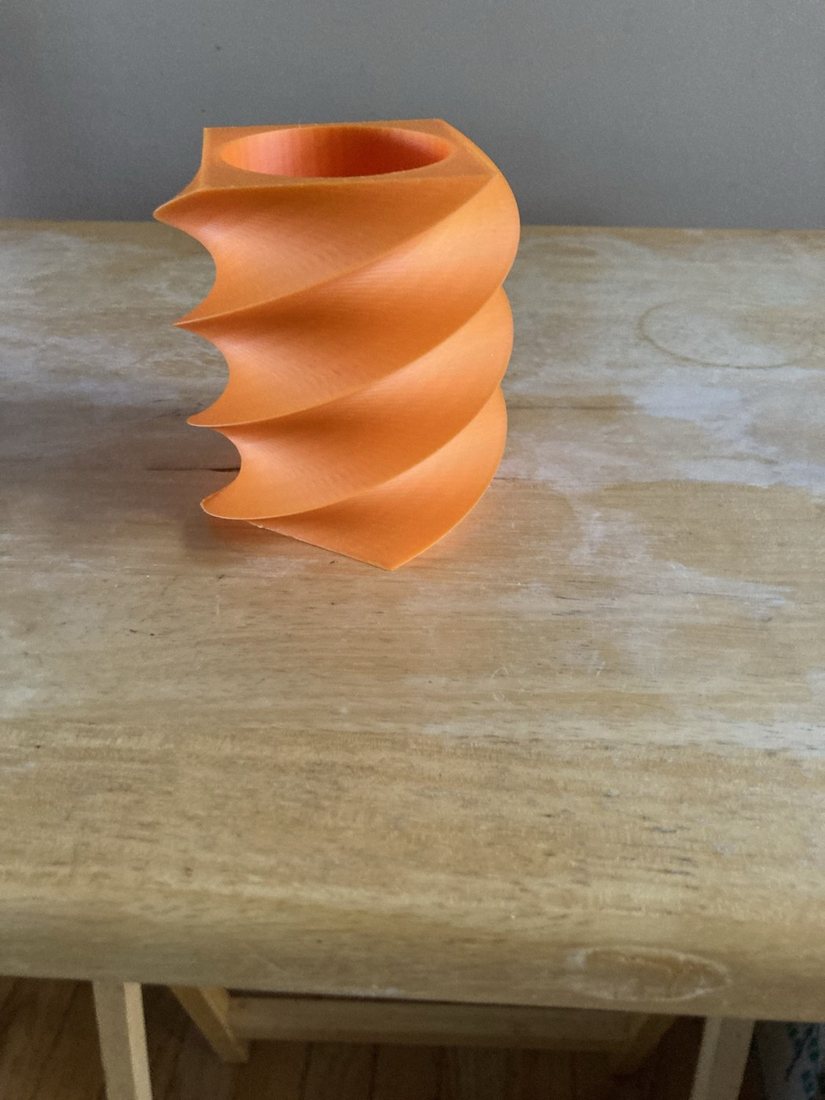 An orange spiral pen holder on a wooden table, seen from the side