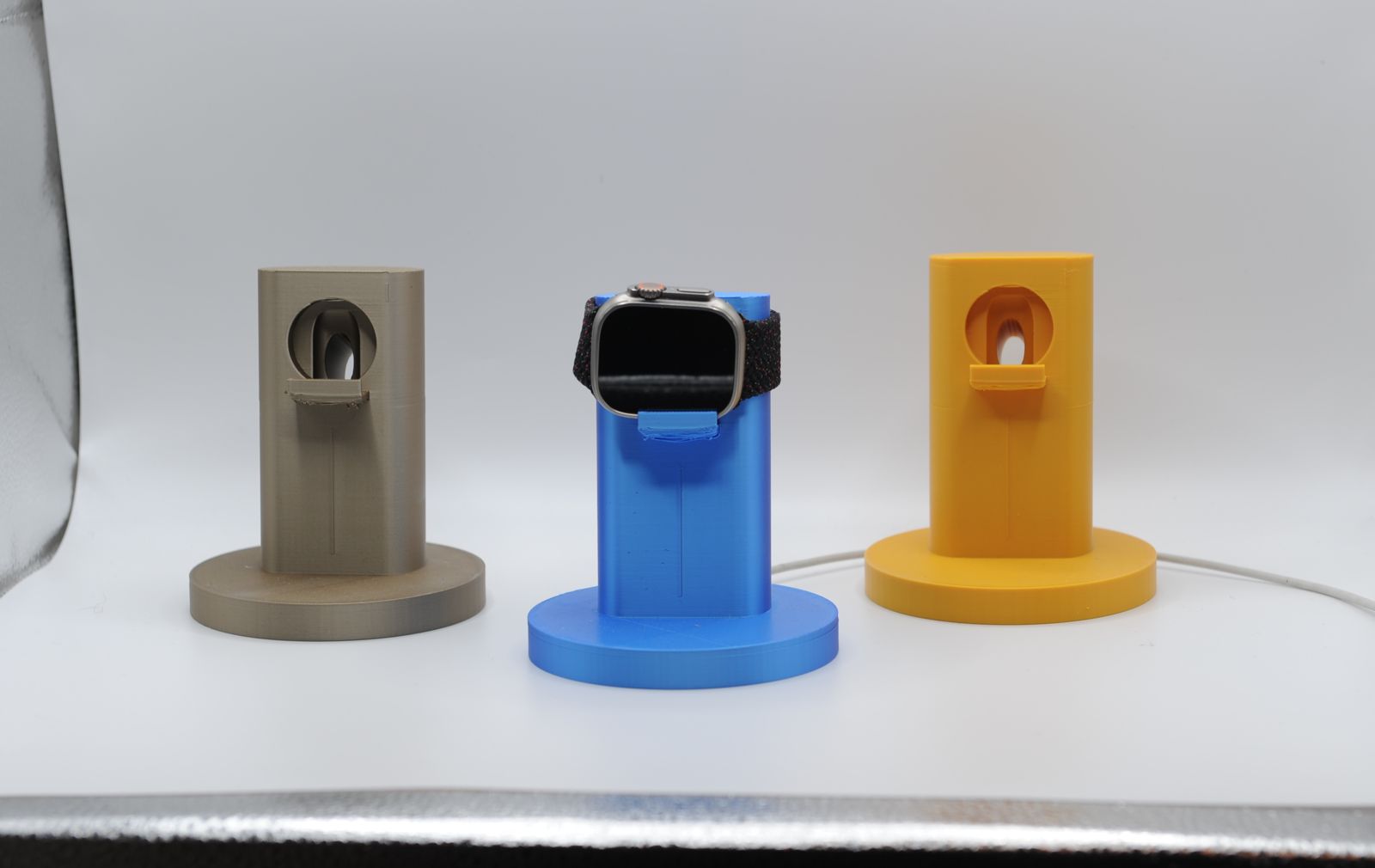 Three watch stands in tan, blue and orange, one holding a watch