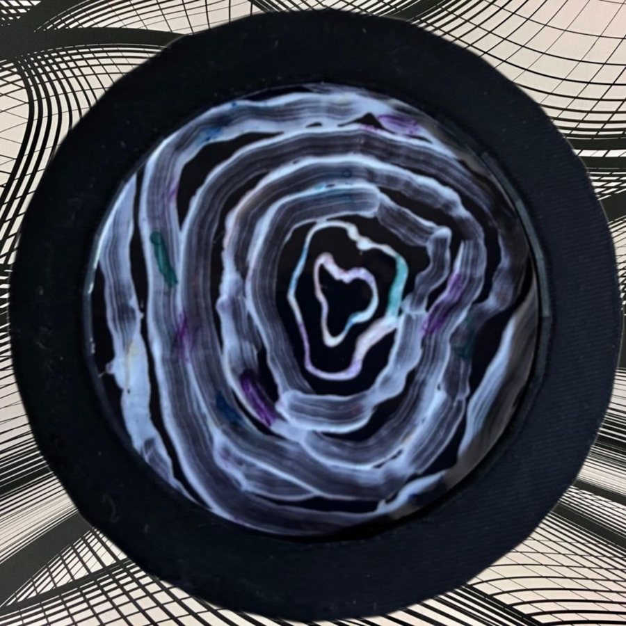 A round coaster printed with an expressive painting of migraine auras, in white swirls on black